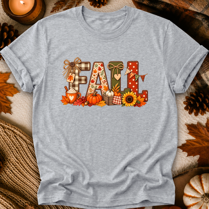 A light heather gray short-sleeve t-shirt with a large 'FALL' graphic on the chest, styled in a flat-lay with autumn props like pinecones, a lit candle, and a knitted blanket.