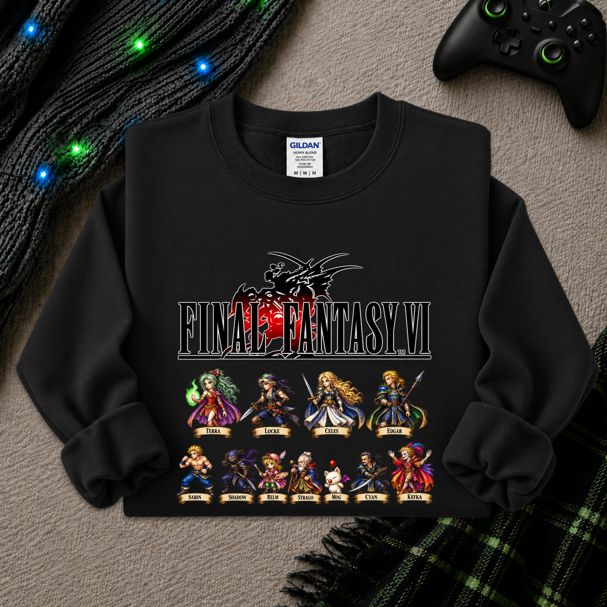 A black long-sleeve sweatshirt with a Final Fantasy VI graphic print, laid flat on a textured gray surface with a game controller, knitted cable lights, and a plaid scarf as styled props.