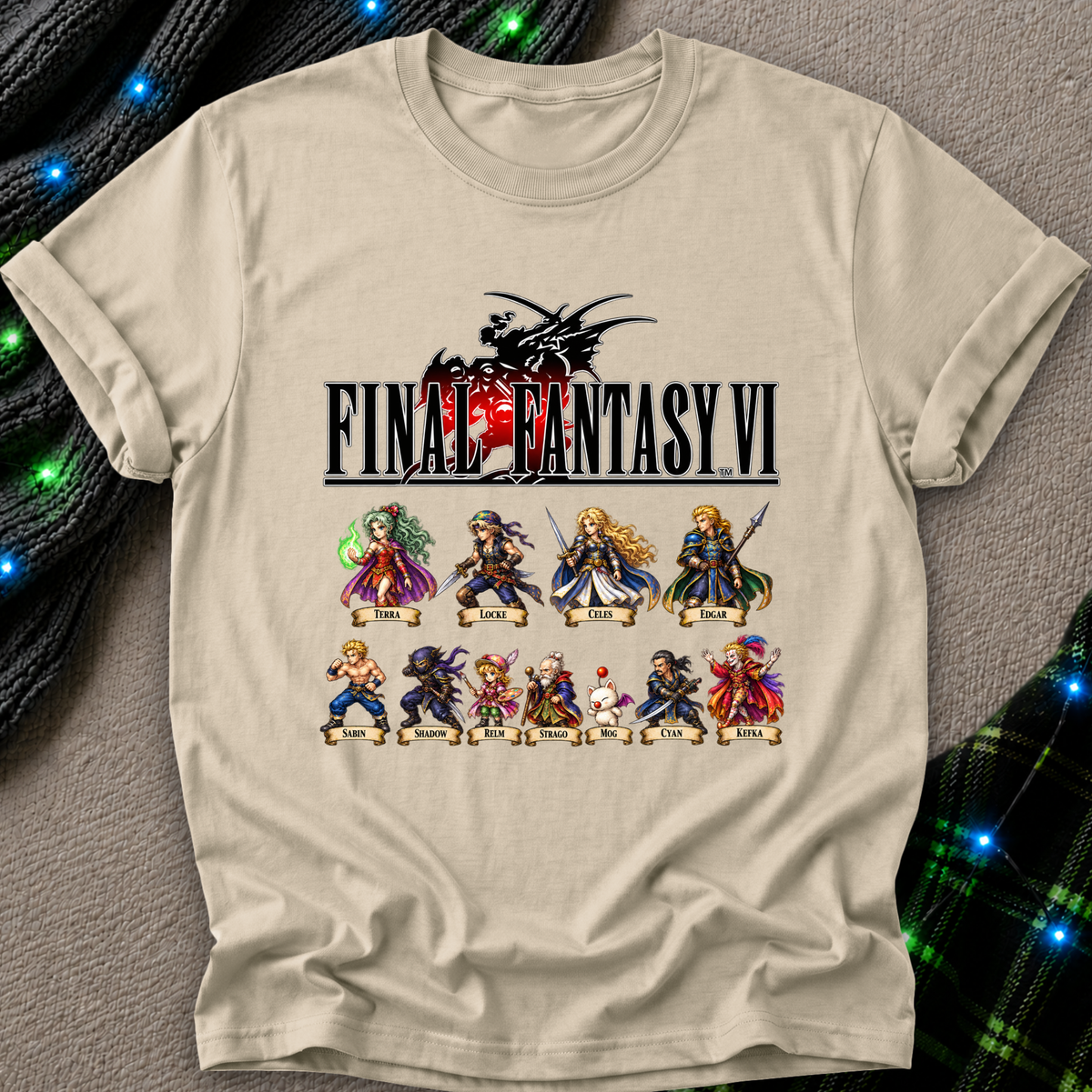 A beige graphic t-shirt featuring the Final Fantasy VI logo and character lineup print, laid flat on a gray textured surface with festive green and blue string lights in the background.