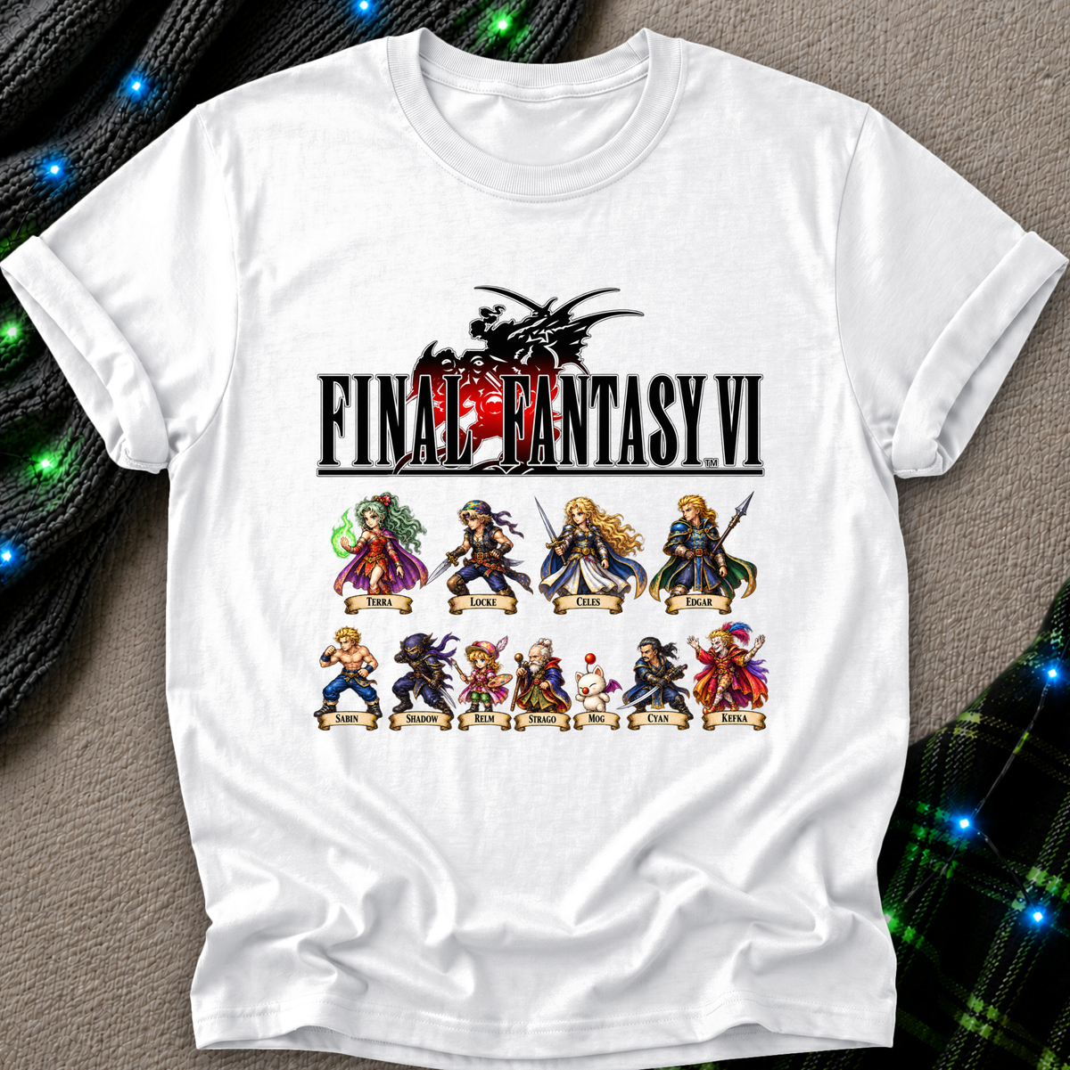 A white short-sleeve t-shirt featuring a graphic print of the Final Fantasy VI logo and character illustrations, laid flat on a textured gray surface with decorative green and black plaid fabric and blue string lights in the background.