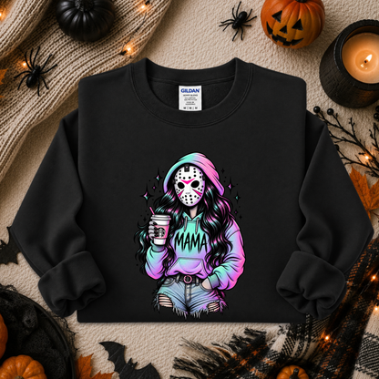 A black crewneck sweatshirt with a colorful graphic of a woman in a hockey mask holding a coffee cup and wearing a 'MAMA' hoodie, styled in a flat lay with Halloween decorations including pumpkins, a candle, and spiderwebs.