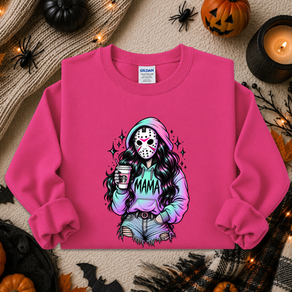 A bright pink crewneck sweatshirt laid flat on a cozy autumn-themed background. The sweatshirt features a colorful graphic of a woman in a hockey mask holding a coffee cup with 'MAMA' written across her hoodie.