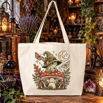 An off-white canvas tote bag with a whimsical witch frog illustration, displayed on a wooden table in a mystical, candle-lit shop setting.