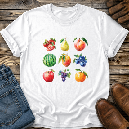 A white short-sleeve crewneck t-shirt featuring a colorful watercolor print of various fruits (strawberries, pear, peach, watermelon, blueberries, apple, grapes, and orange) arranged in a grid. The shirt is displayed in a flat-lay composition on a rustic wooden surface, styled with blue jeans, brown leather shoes, and leather gloves.