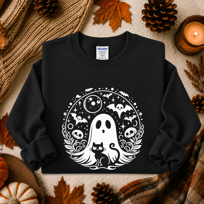 A black crewneck sweatshirt with a white circular graphic of a ghost, cat, bats, skulls, and moon, styled in an autumn flat-lay with pinecones, leaves, a candle, and a knit blanket.