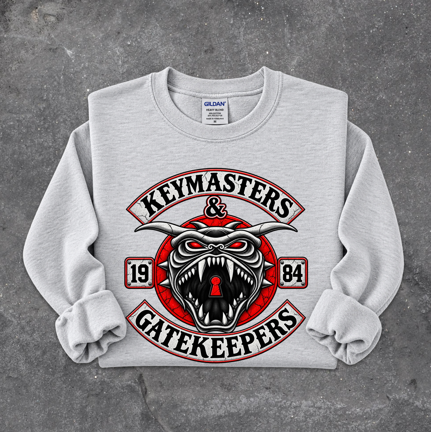 A light gray crewneck sweatshirt with rolled cuffs, featuring a large graphic print on the front. The graphic displays a stylized red, black, and white horned snake head with the words 'KEYMASTERS & GATEKEEPERS' in arched lettering, with '19' and '84' on either side.