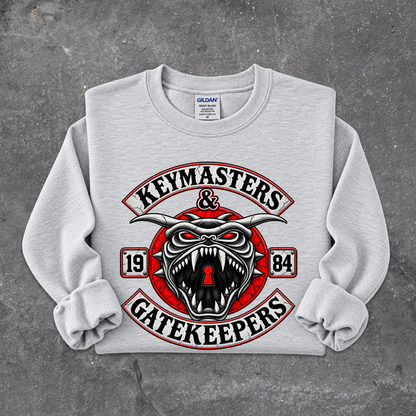 A light gray crewneck sweatshirt with rolled cuffs, featuring a large graphic print on the front. The graphic displays a stylized red, black, and white horned snake head with the words 'KEYMASTERS & GATEKEEPERS' in arched lettering, with '19' and '84' on either side.