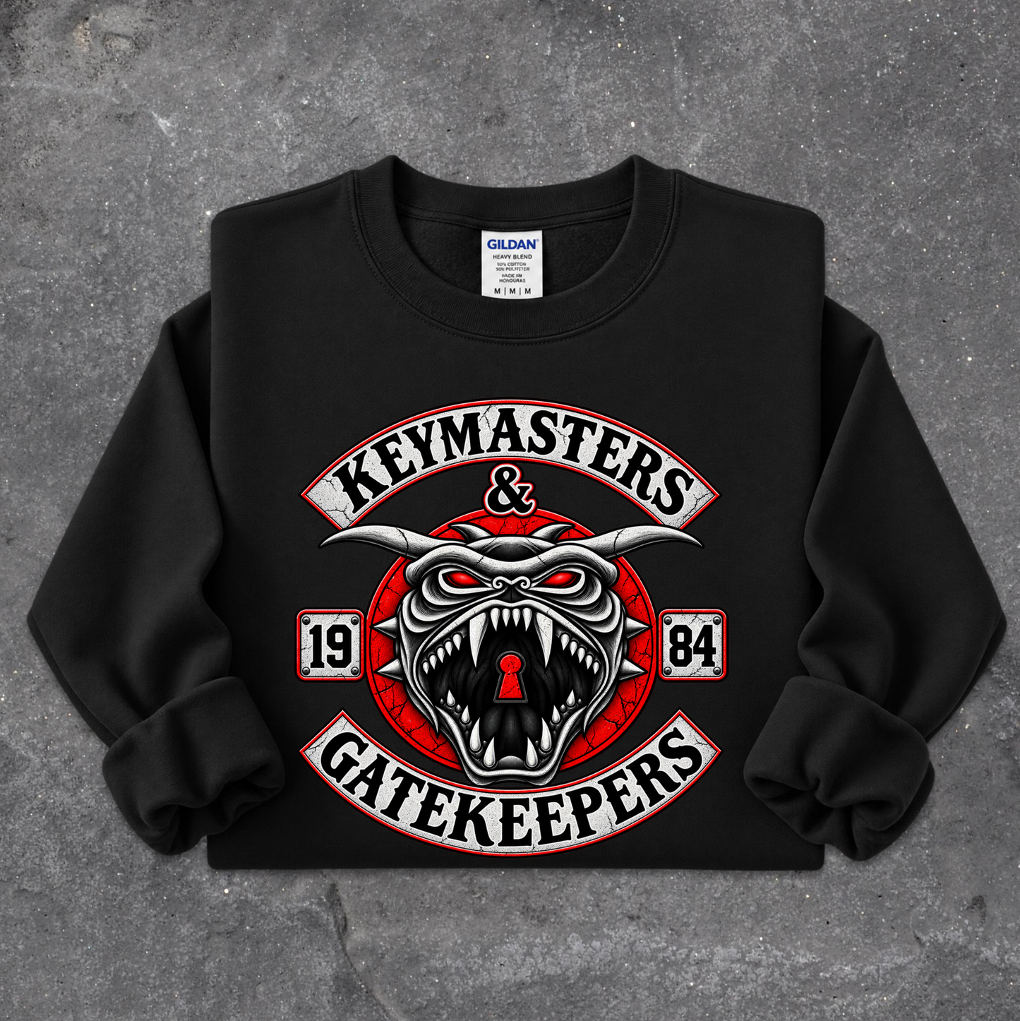 A black crewneck sweatshirt with a large graphic print on the front reading 'KEYMASTERS & GATEKEEPERS' in white and red, featuring a snarling horned face with a keyhole in the mouth. The sweatshirt is laid flat on a textured gray concrete surface.