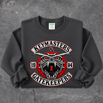 A dark gray crewneck sweatshirt featuring a large graphic print of a snarling horned devil with the words 'KEYMASTERS & GATEKEEPERS' and '1984' on a textured gray background.