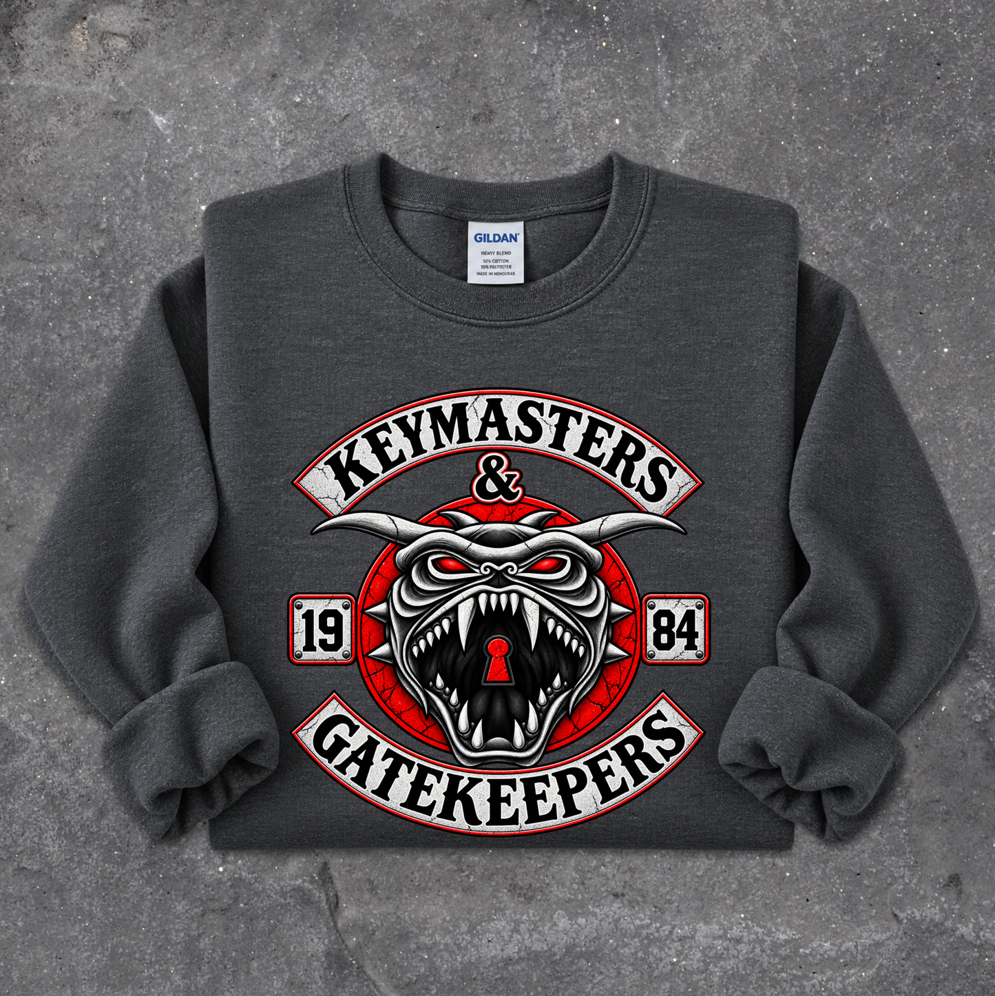 A dark gray crewneck sweatshirt featuring a large graphic print of a snarling red and white horned creature with the words 'KEYMASTERS & GATEKEEPERS' and '1984' on a textured gray background.