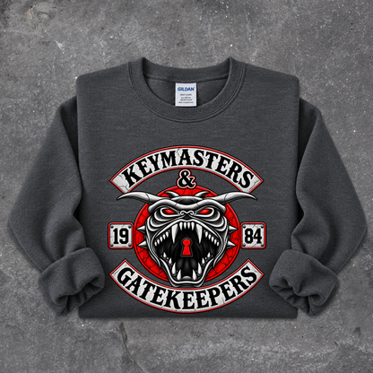 A dark gray crewneck sweatshirt featuring a large graphic print of a snarling red and white horned creature with the words 'KEYMASTERS & GATEKEEPERS' and '1984' on a textured gray background.