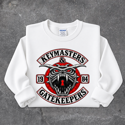 A white long-sleeve crewneck sweatshirt with a large graphic print on the front. The graphic features a red and black snarling horned demon face with a keyhole in its mouth, surrounded by the words 'KEYMASTERS & GATEKEEPERS' in an arch, with '1984' on either side.