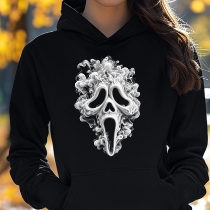 A person wearing a black pullover hoodie with a large white and gray smoke-mask graphic on the chest, photographed outdoors with blurred autumn foliage in the background.