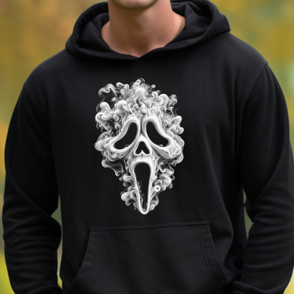 A person wearing a black pullover hoodie with a large white ghost-face style graphic on the chest, shown against a softly blurred outdoor background.