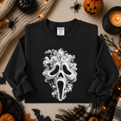 A black crewneck sweatshirt featuring a white and gray smoke graphic of the Ghostface mask from the Scream franchise, styled in a cozy Halloween flat-lay with pumpkins, a candle, and spider decorations.