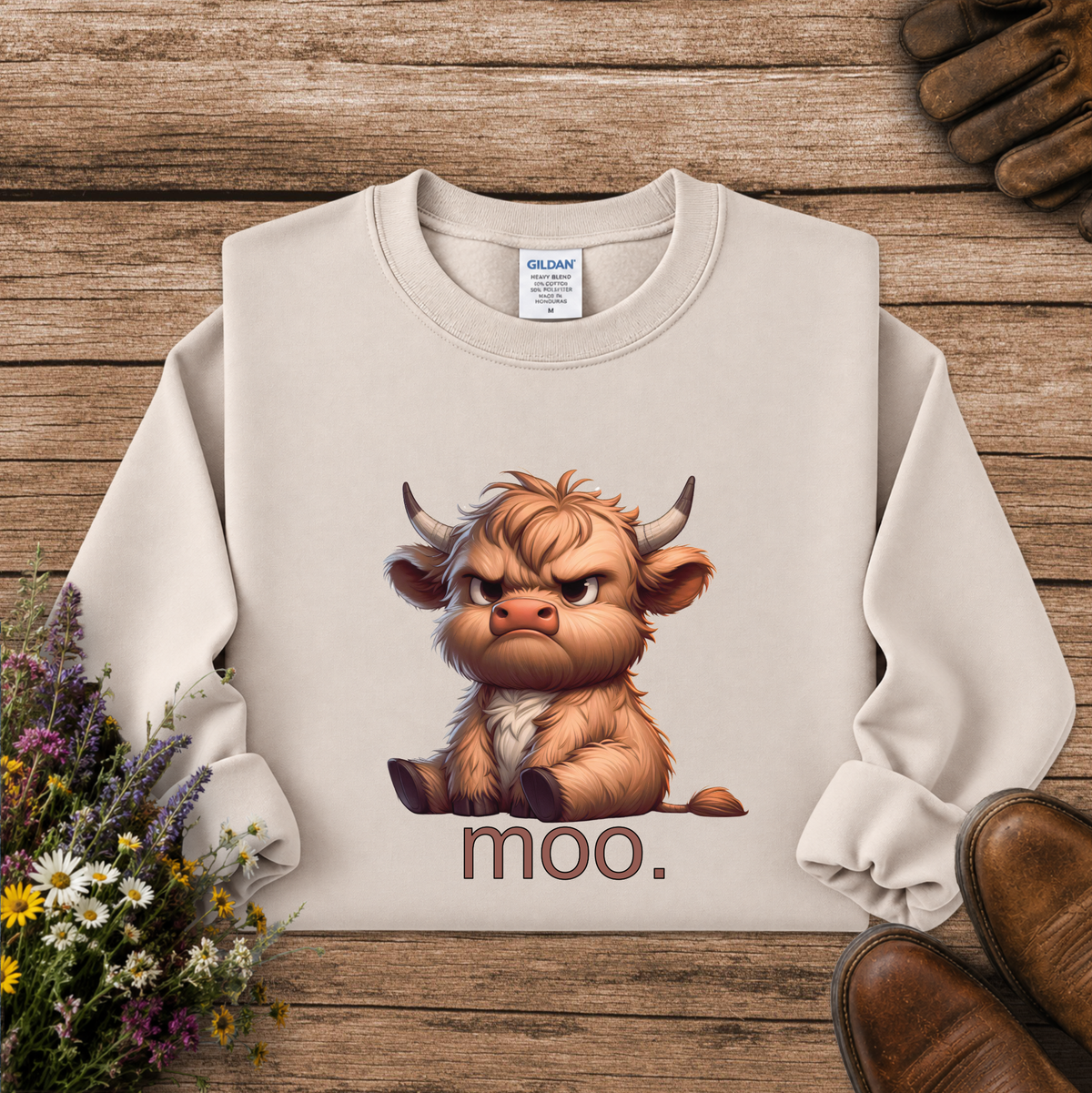 A cream-colored crewneck sweatshirt featuring a cartoon illustration of an angry Highland cow with the word 'moo.' printed below it.