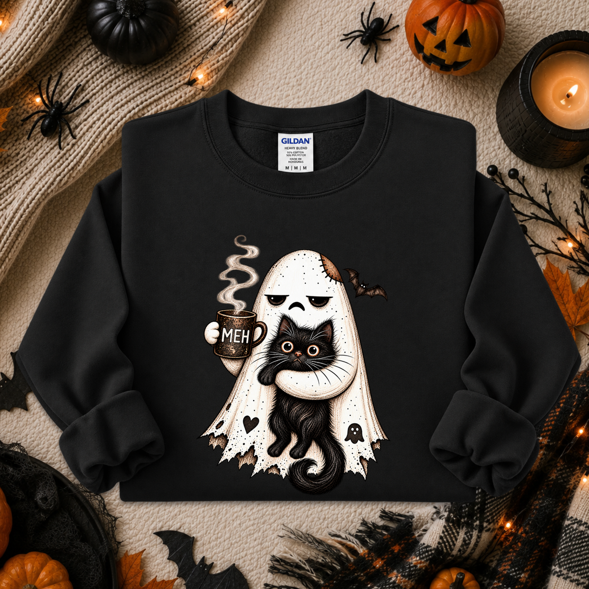A black crewneck sweatshirt with a Halloween graphic of a ghost holding a black cat with the text 'MEH', styled in a flat lay with autumn and Halloween props.