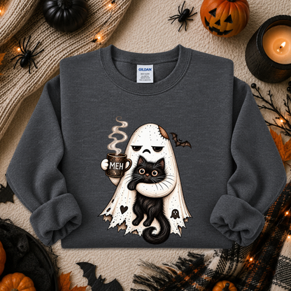 A dark gray crewneck sweatshirt featuring a cute graphic of a white ghost with a skull face holding a black cat and a mug that says 'MEH'. The sweatshirt is presented in a flat-lay Halloween setting with pumpkins, spider decorations, and a candle.