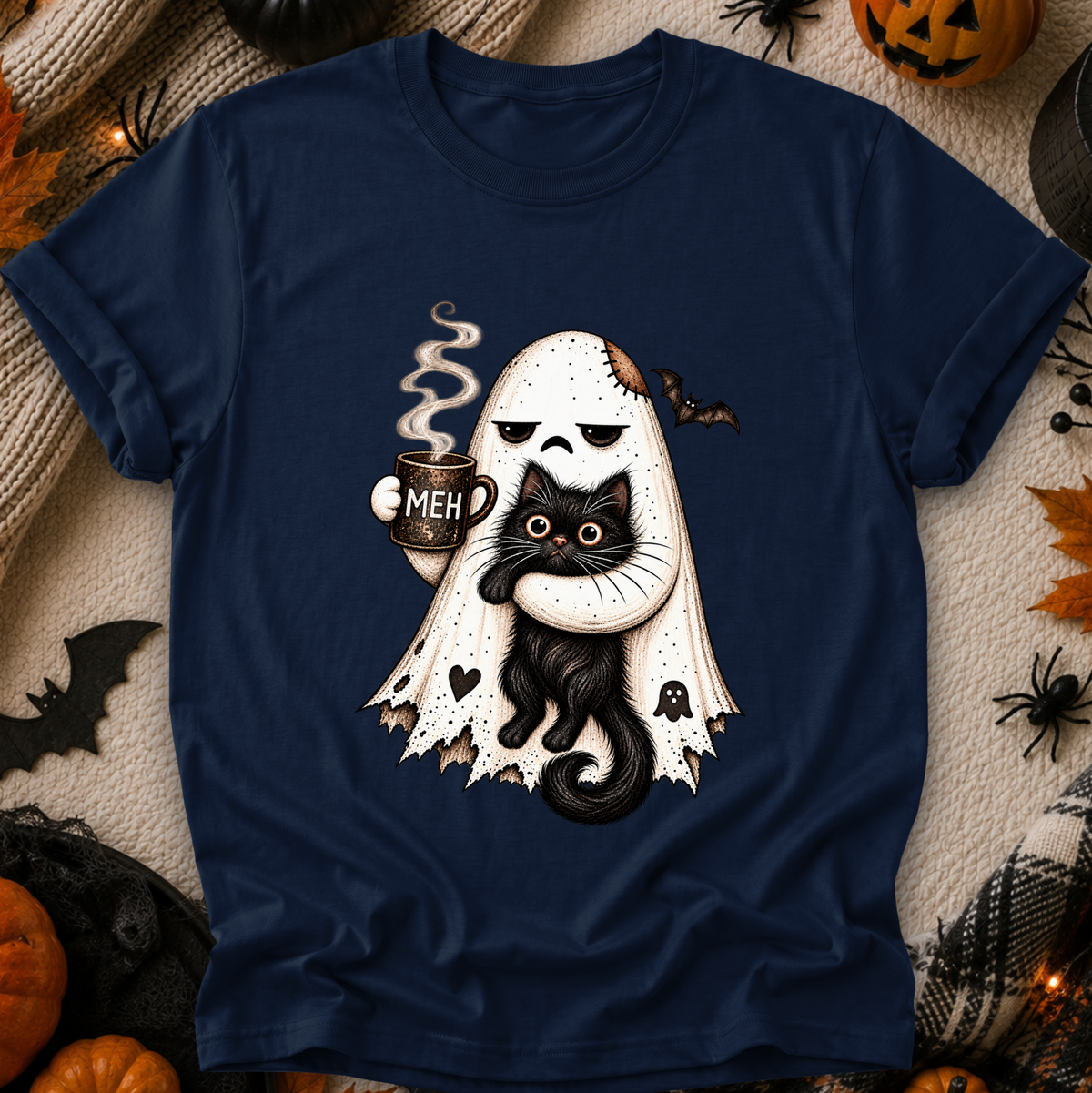 A navy blue short-sleeve t-shirt with a Halloween graphic of a ghost hugging a black cat, styled in a flat-lay with autumn and Halloween props.