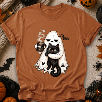 A rust-orange crewneck t-shirt featuring a cute Halloween graphic of a white ghost hugging a black cat while holding a mug that says 'MEH'. The shirt is displayed in a flat-lay arrangement surrounded by seasonal props like pumpkins, spiderwebs, and a cozy blanket.