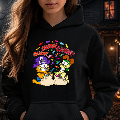 A woman wearing a black hoodie with a colorful cartoon graphic of Garfield and his cat buddies overflowing with candy, with the word 'CANDY!' repeated above them. The background is a softly blurred outdoor nighttime scene with warm lights.