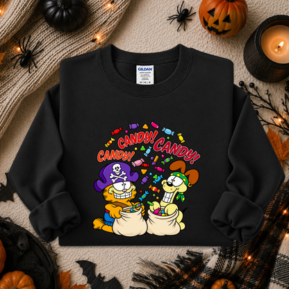 A black long-sleeve crewneck sweatshirt featuring a colorful cartoon graphic of Garfield and Odie with candy bags and the text 'CANDY! CANDY!' in red. The sweatshirt is displayed in a flat-lay Halloween setting with pumpkins, a candle, and spider decorations.