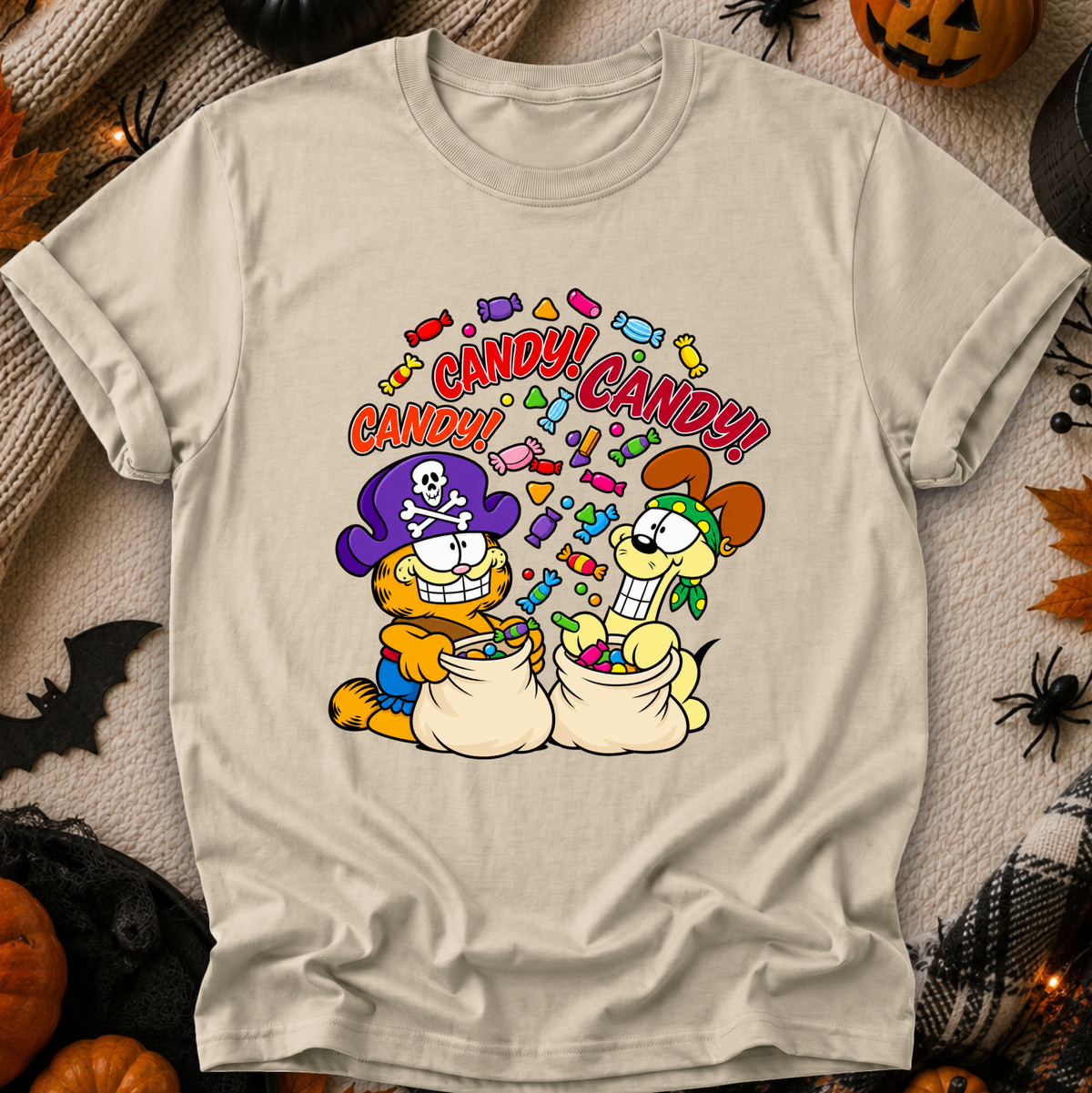A beige graphic t-shirt featuring Garfield and Odie as pirates filled with candy, surrounded by Halloween decorations like pumpkins and spiderwebs.