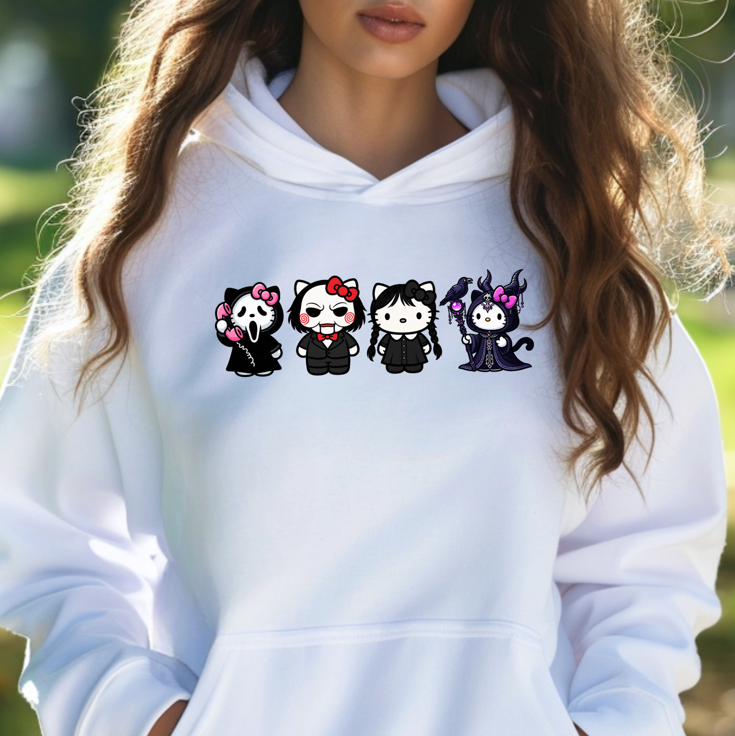 A woman wearing a white pullover hoodie with a graphic print of four cute cartoon characters in black outfits across the chest, set against a blurred green outdoor background.