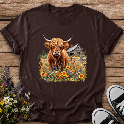 brown tshirt with a graphic of a highland cow standing in a field of wildflowers in front of a barn