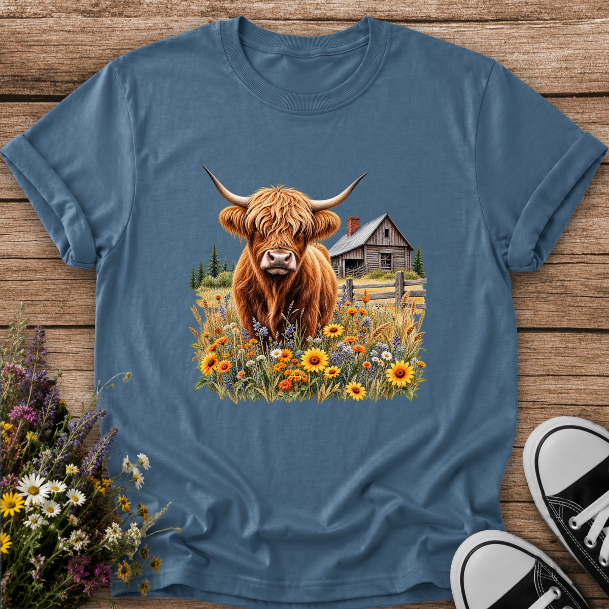 blue tshirt with a graphic of a highland cow standing in a field of wildflowers in front of a barn