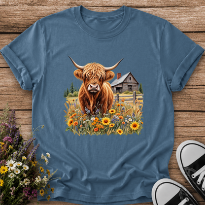 blue tshirt with a graphic of a highland cow standing in a field of wildflowers in front of a barn