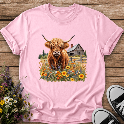 pink tshirt with a graphic of a highland cow standing in a field of wildflowers in front of a barn