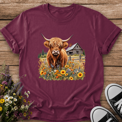 maroon tshirt with a graphic of a highland cow standing in a field of wildflowers in front of a barn