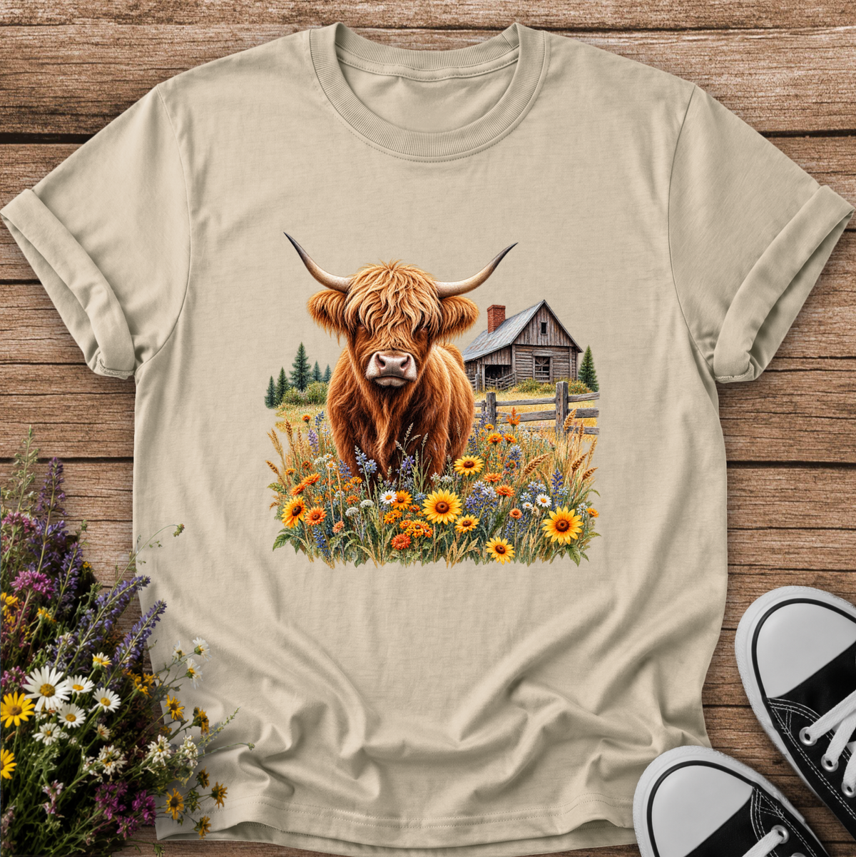 beige tshirt with a graphic of a highland cow standing in a field of wildflowers in front of a barn