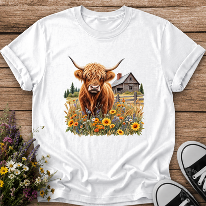 white tshirt with a graphic of a highland cow standing in a field of wildflowers in front of a barn