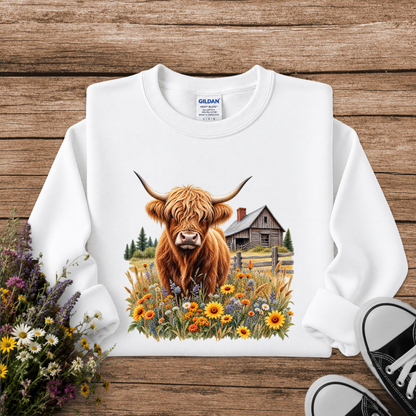 white sweatshirt with a graphic of a highland cow standing in a field of wildflowers in front of a barn