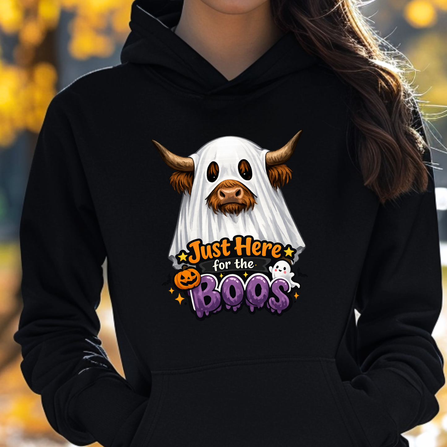 woman wearing a black sweatshirt with a highland cow wearing a halloween ghost costume and says just here for the boos