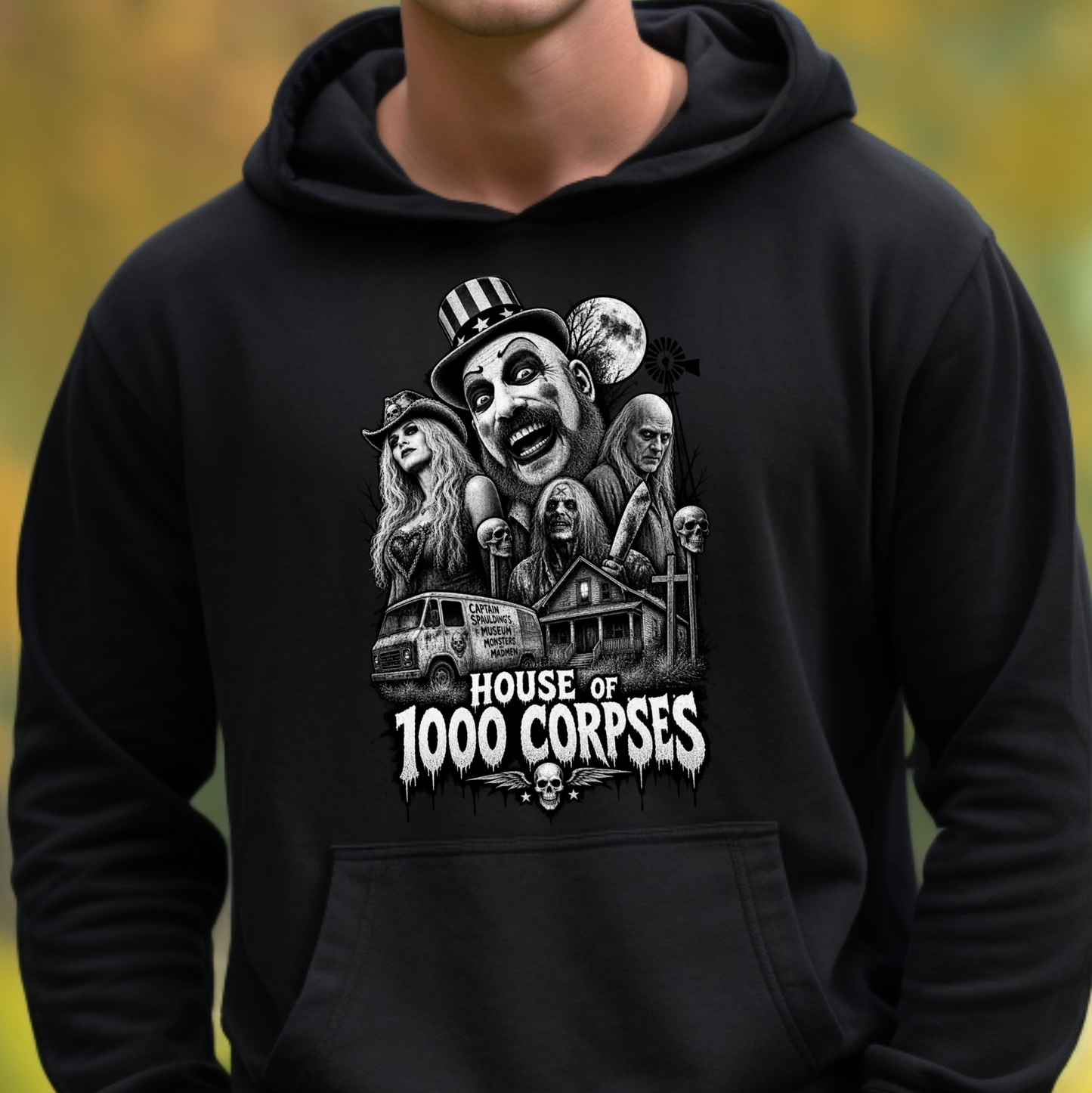 A person wearing a black pullover hoodie with a large white horror-themed graphic on the chest reading 'HOUSE OF 1000 CORPSES,' shown against a blurred outdoor background.