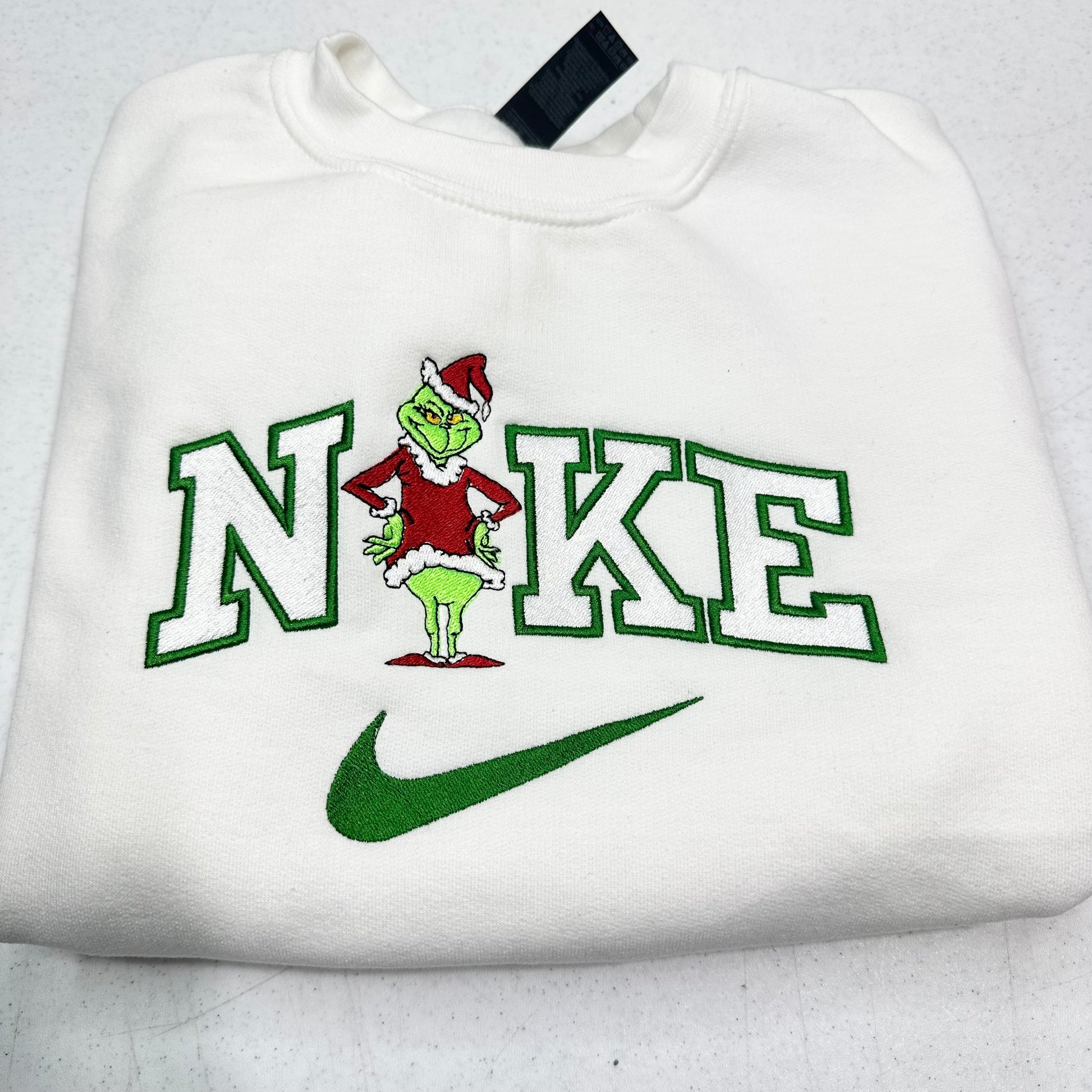 White sweatshirt with a grinch design and 'Nike' logo on a light gray background