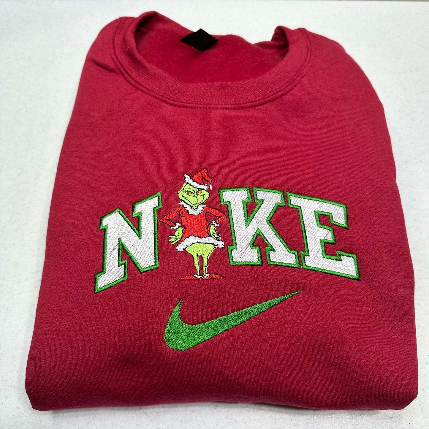 Folded red sweatshirt with a grinch design on a white background