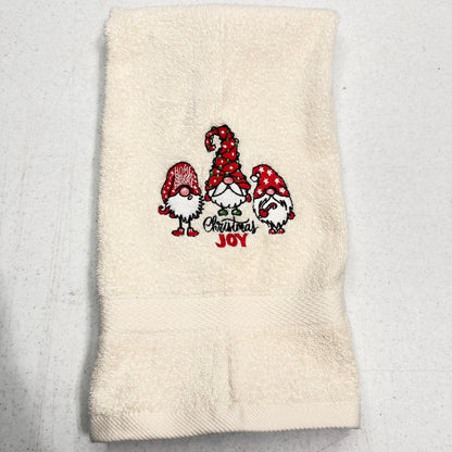 An off-white terry cloth hand towel featuring an embroidered design of three Christmas gnomes and the words 'Christmas Joy' in red and black.