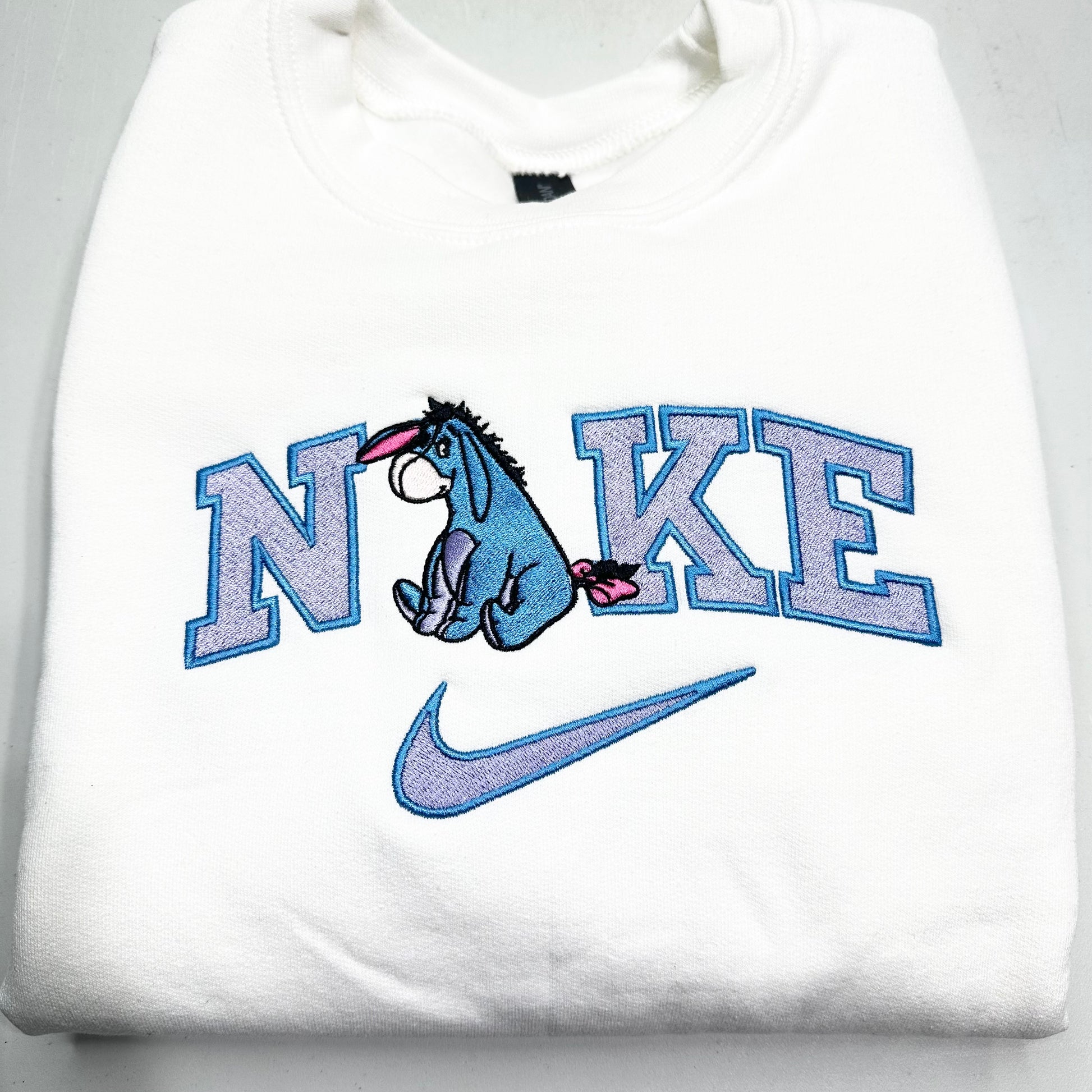 embroidered eeyore in the nike logo on a white sweatshirt
