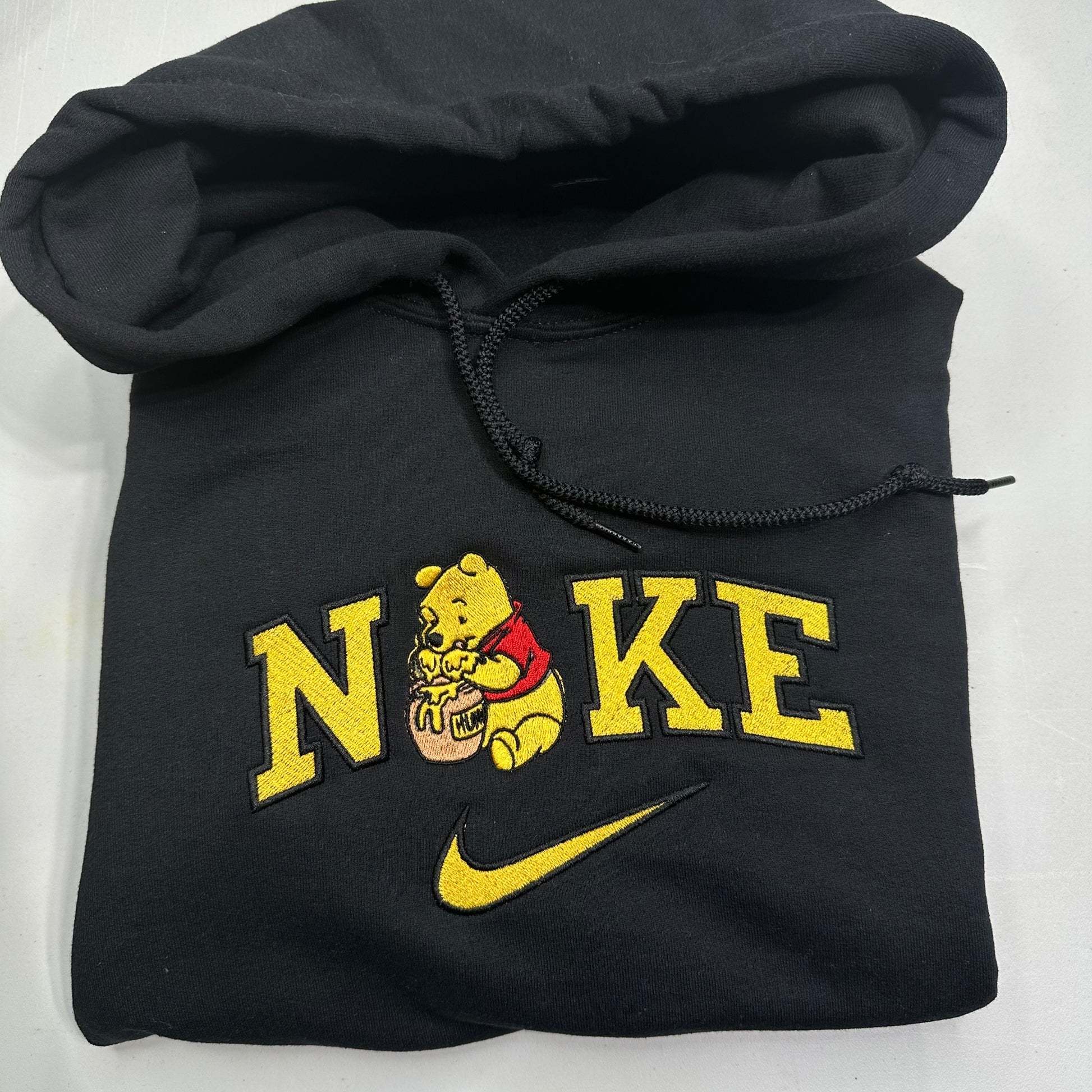 black sweatshirt with embroidered winnie the pooh in the middle of the nike logo