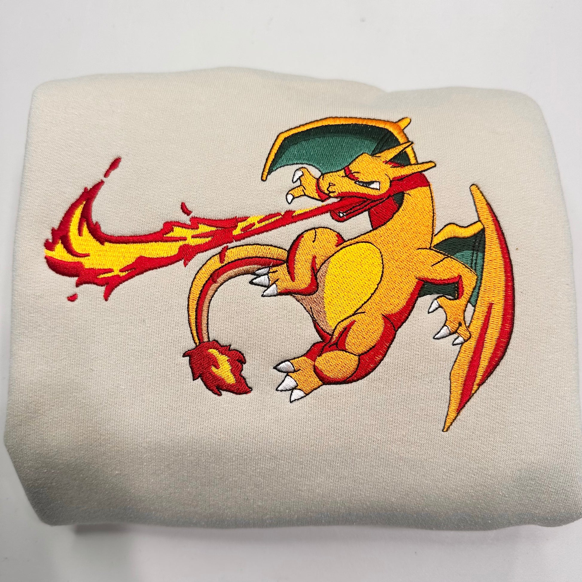 beige sweatshirt with embroidered pokemon charizard character blowing flames 