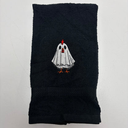 A black cotton towel featuring an embroidered cartoon ghost chicken in the center. The ghost has a white body, black eyes, a red comb, and orange feet.