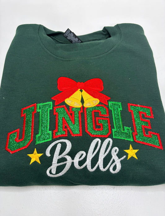 A folded dark green crewneck sweatshirt featuring a glittery 'JINGLE Bells' graphic on the front, complete with a red bow, gold bells, and yellow stars.