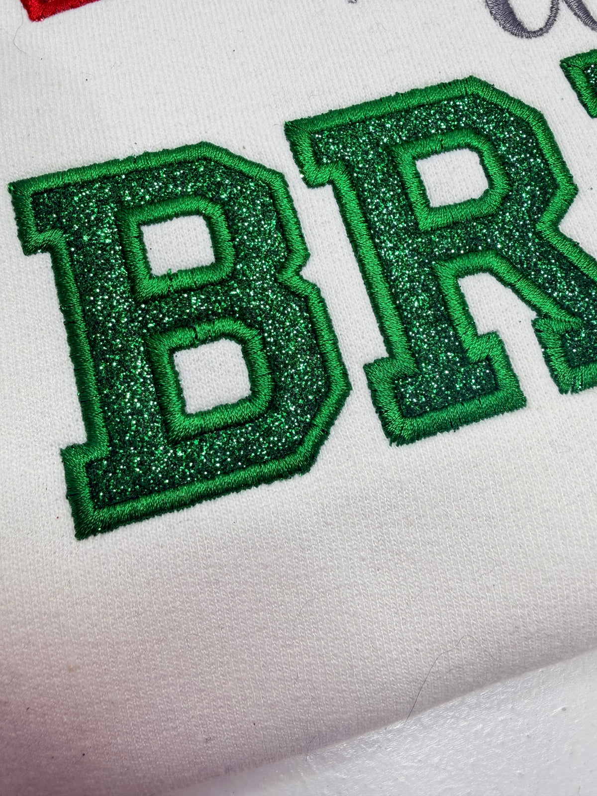 close up of embroidered text with green glitter applique