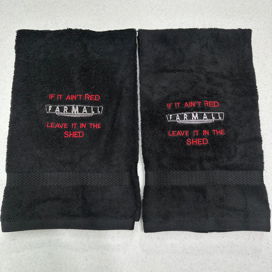 Two black towels laid flat on a light gray surface, each embroidered with the phrase 'IF IT AIN'T RED FARMALL LEAVE IT IN THE SHED' in red and white.
