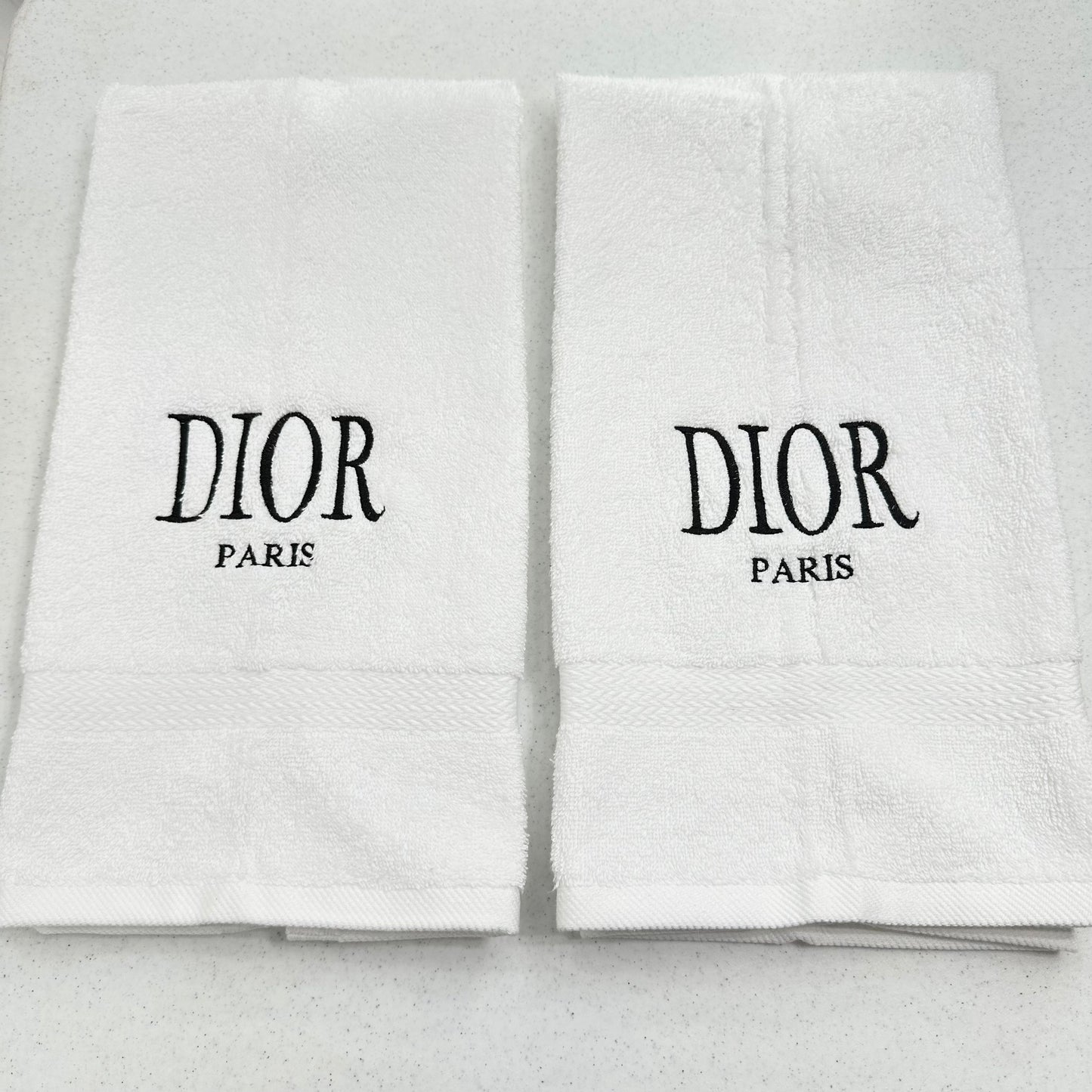 Two white Dior towels with black text on a light gray background