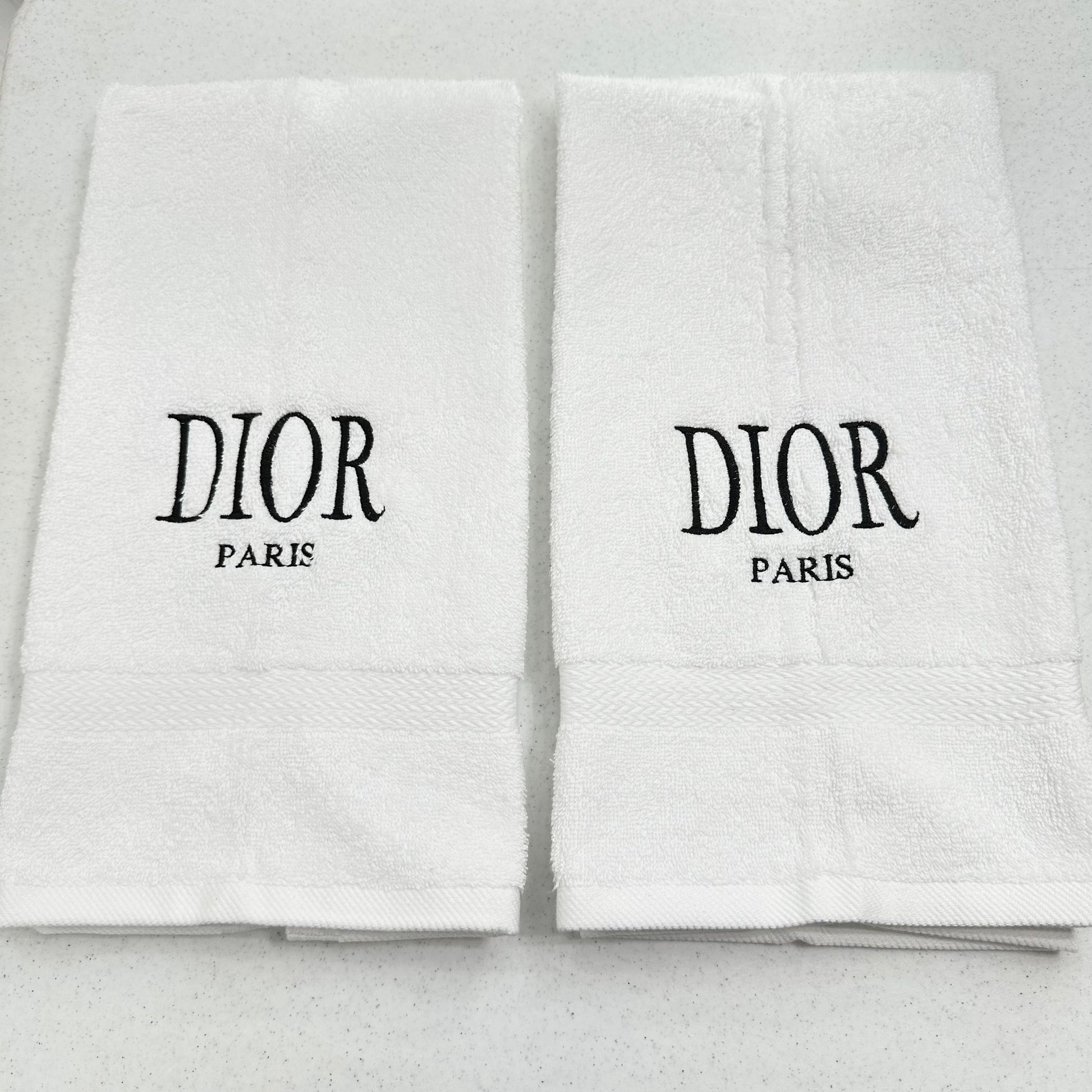 Two white Dior towels with black text on a light gray background